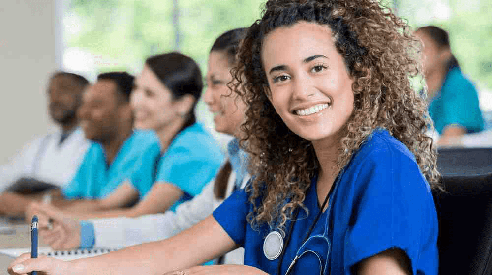 Medical school students in a classroom wearing scrubs.